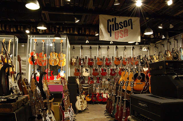 店内に入って右手、ギブソン・フラッグの下にはギブソンSG、レス・ポールJr、最近扱うようになったというアコースティック・ギターなどが並ぶ。